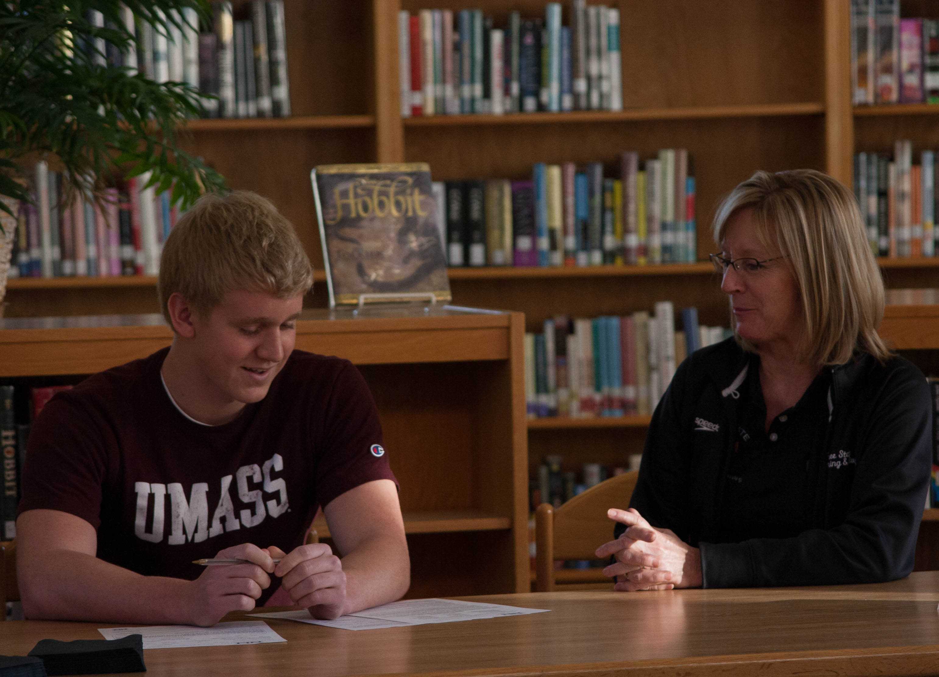 Senior Ben Sloan signs to swim at the University of Massachusetts in the Free State library in December. Coach Annette McDonald looks on from his side.